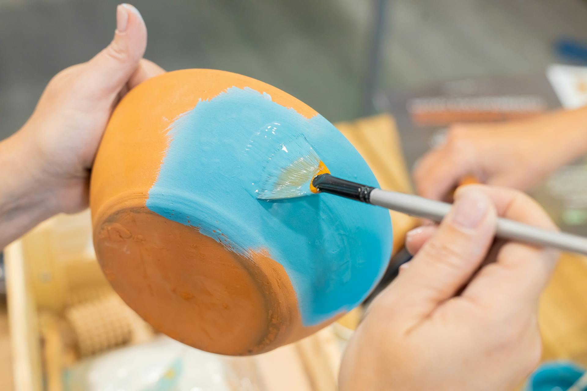 Hands painting a ceramic bowl blue, showcasing artistic detail and creativity.