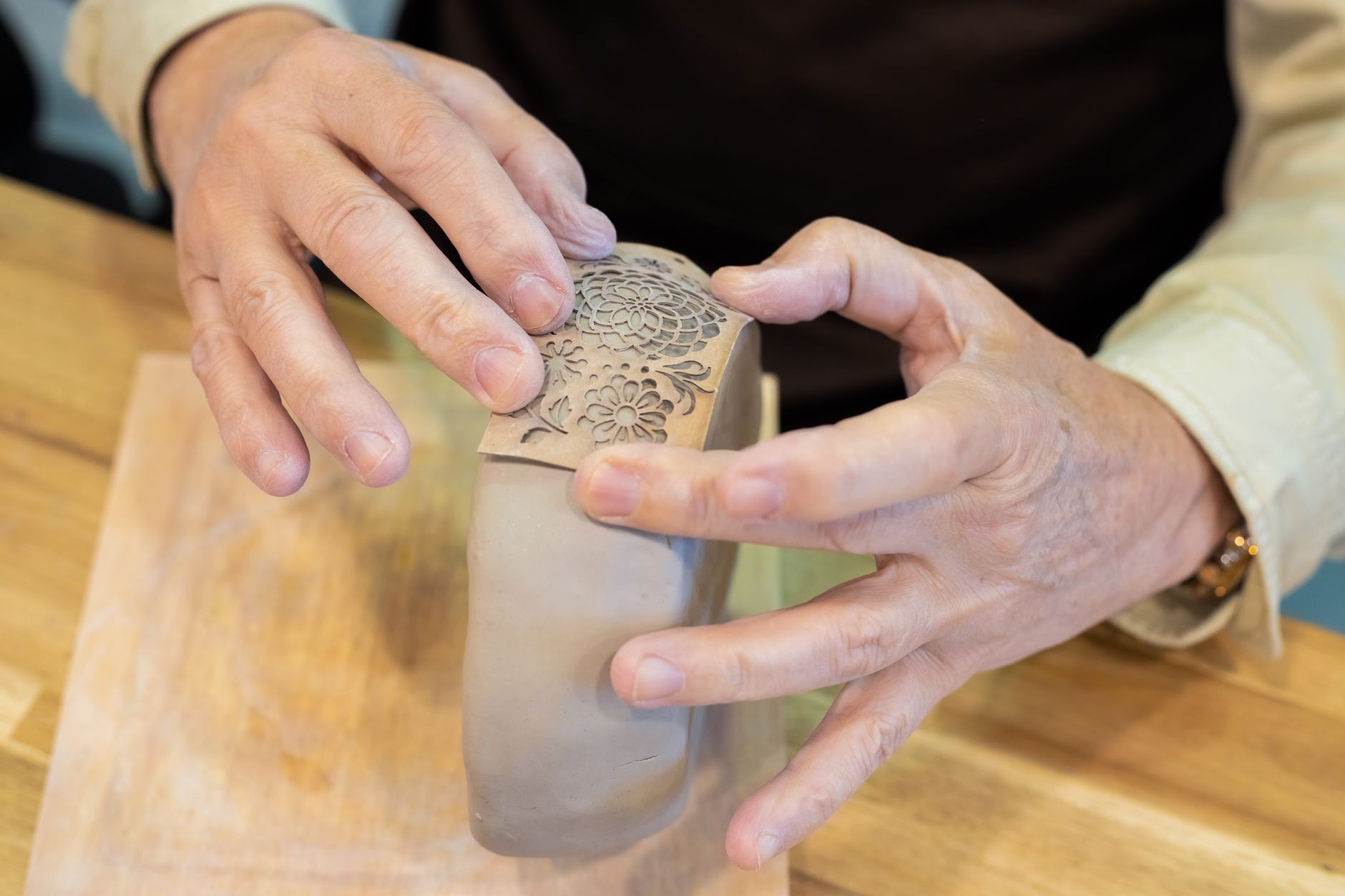 Close-up of hands molding and decorating a clay pot, showcasing craftsmanship in pottery making.