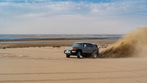 Free Modern SUV car drifting on sandy dunes near sea against cloudy blue sky in desert Stock Photo