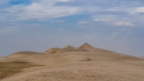 Free Picturesque scenery of tall sandy dunes under cloudy blue sky in endless desert on sunny day Stock Photo
