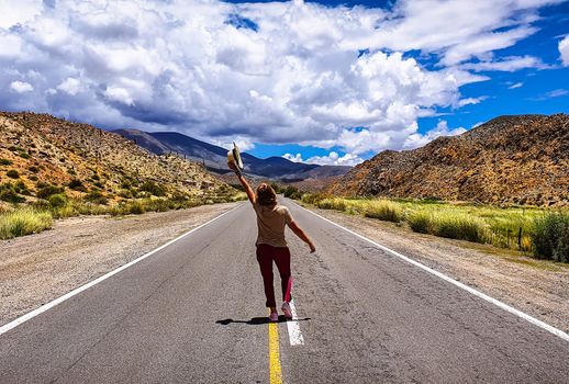 A woman joyfully runs on a mountain road under a bright blue sky, embracing freedom and adventure.