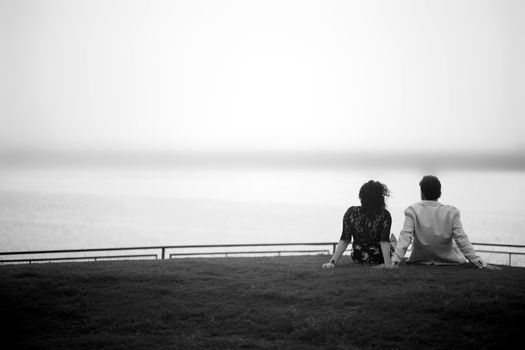 A romantic black-and-white photo of a couple sitting together by the sea, expressing love and togetherness.