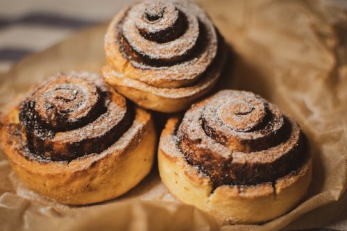Free Close-up of three freshly baked cinnamon rolls dusted with powdered sugar on brown paper. Stock Photo
