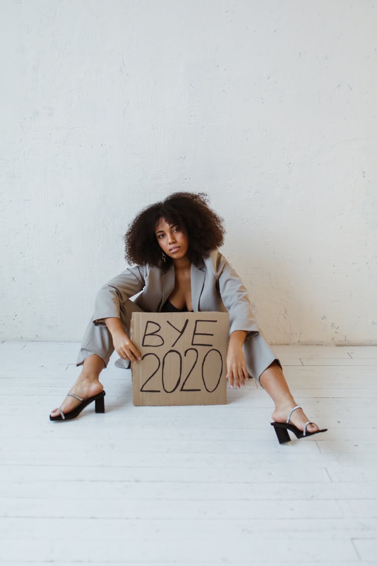 A Woman Sitting On The Floor Holding A Sign