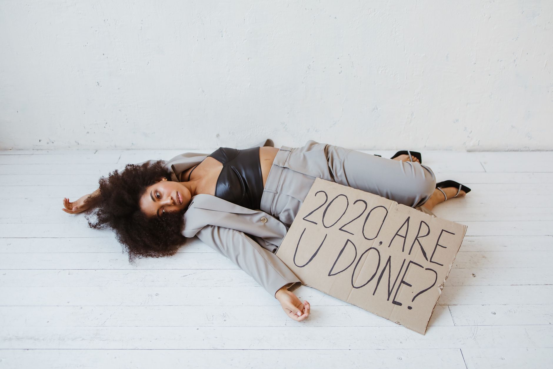 Woman in business suit lying on floor with sign "2020 Are U Done?"