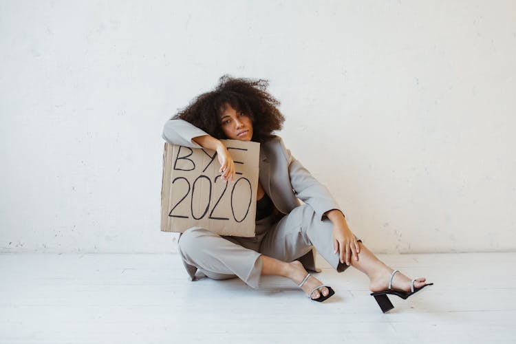 A Woman Sitting On The Floor Holding A Sign