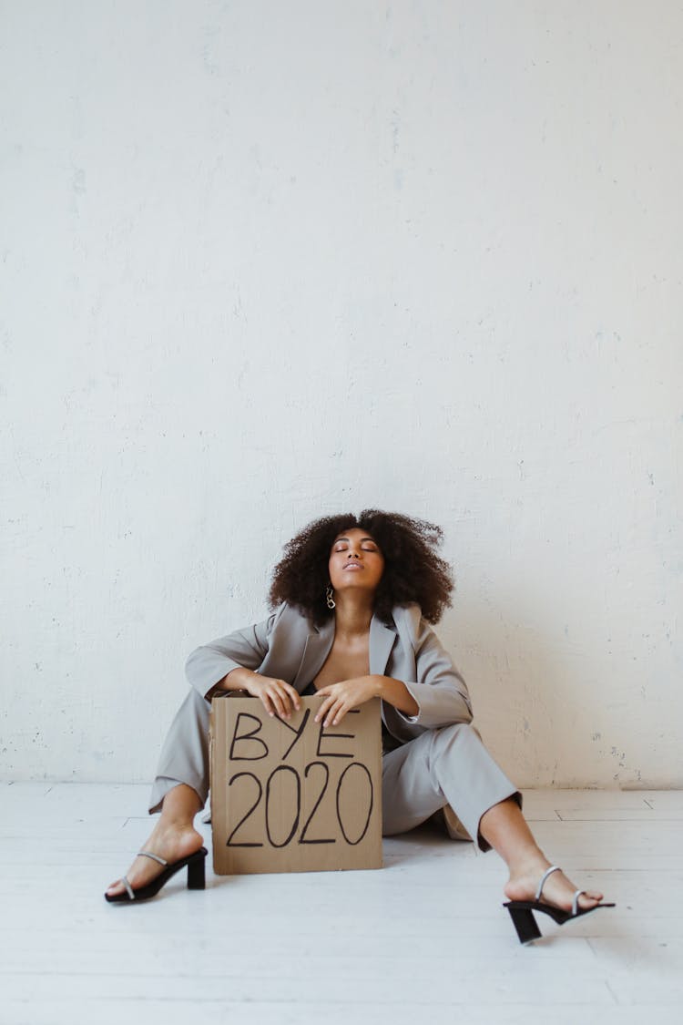 A Woman Sitting On The Floor Holding A Sign