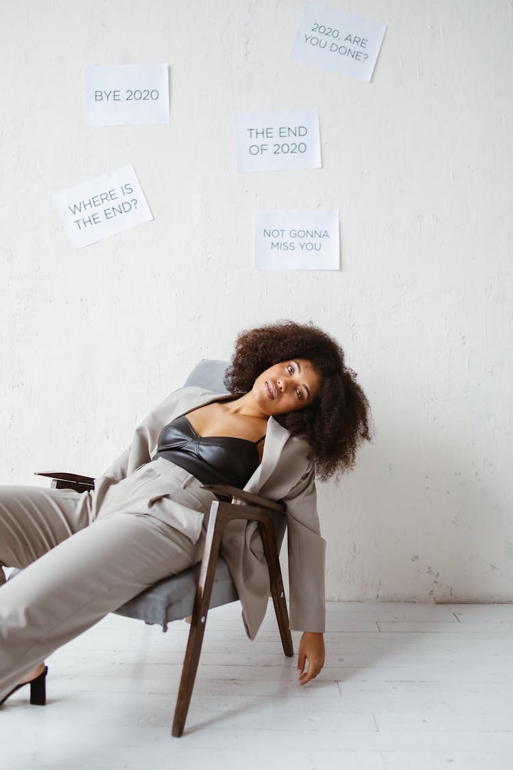 A Tired Woman Sitting On A Chair Beside A Wall With Posted Signs About 2020