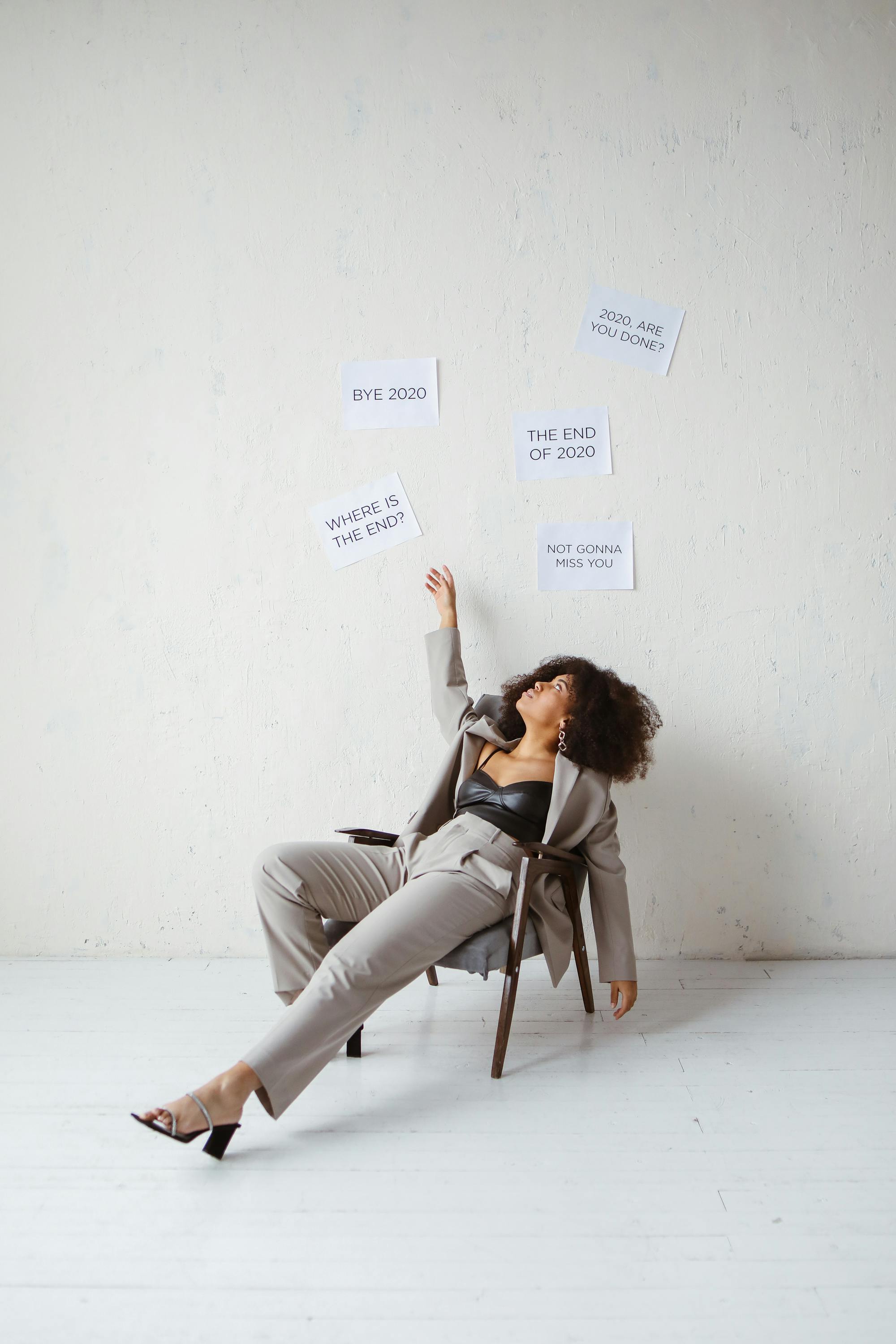 A woman in a suit symbolizing burnout, sitting under papers labeled 2020 on a white backdrop.