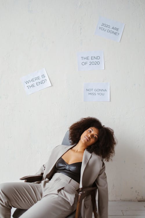 A Woman Sitting on a Chair Beside a Wall with Posted Signs About 2020
