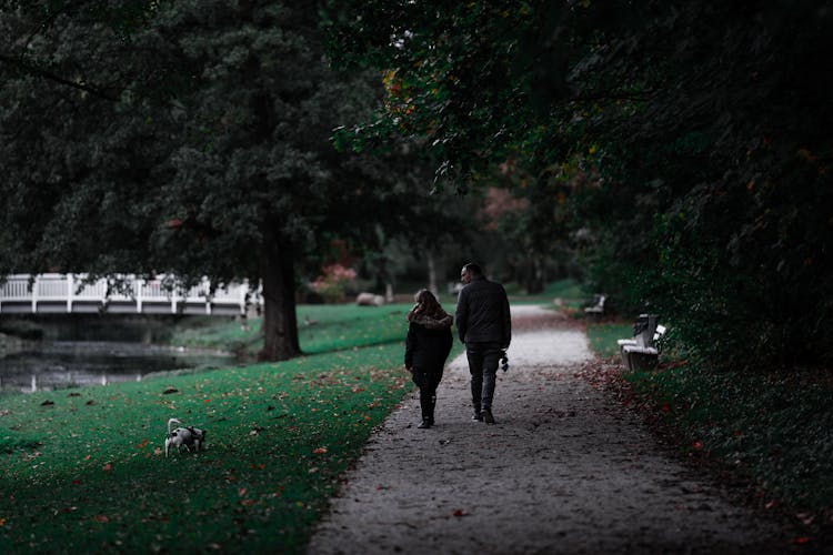 Couple Walking On Pathway With Their Dog On The Grass