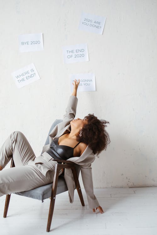 Free A Woman Sitting on a Chair Beside a Wall with Posted Signs About 2020
 Stock Photo