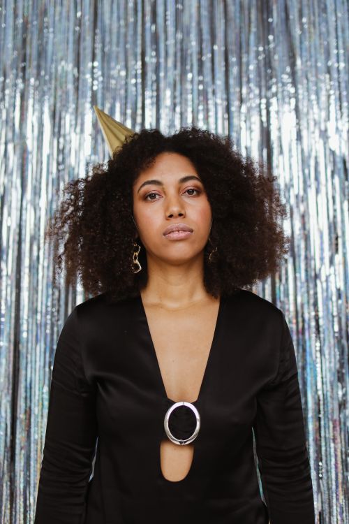 Free Stylish young woman with afro hair and party hat posing against shimmering backdrop. Stock Photo