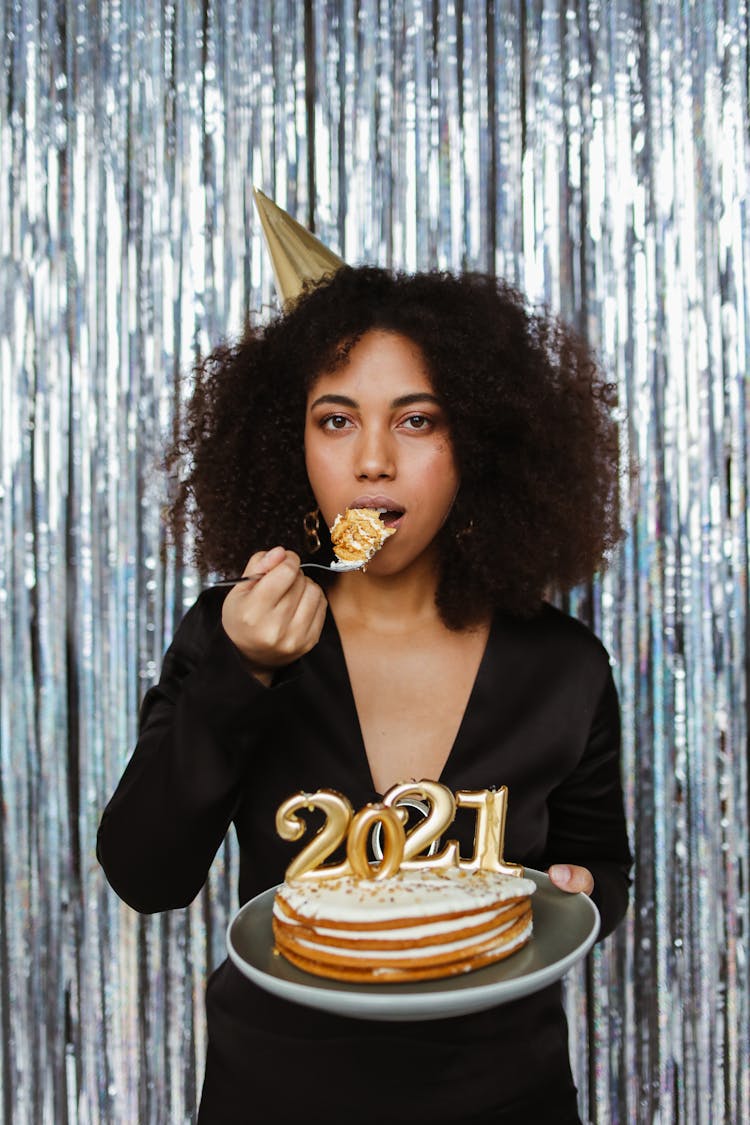 Woman In Black Long Sleeves Eating A Cake While Looking At The Camera