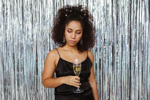 Free Stylish woman in a black dress holding a champagne glass against a silver backdrop. Stock Photo
