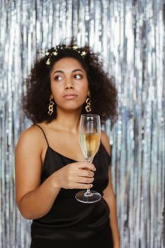 Stylish woman in black dress holding a champagne glass in front of a shimmering background.