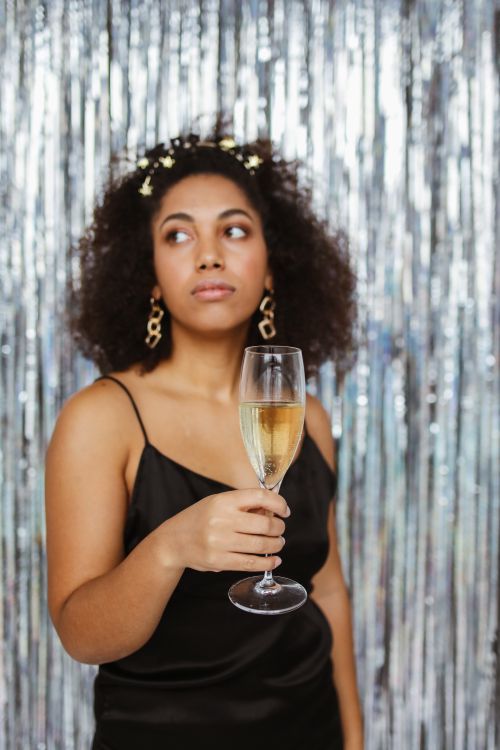 Free Stylish woman in black dress holding a champagne glass in front of a shimmering background. Stock Photo