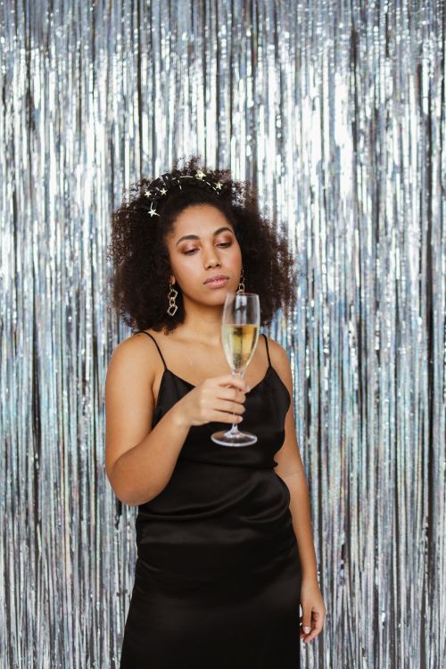 Free Black woman with afro hair holding a champagne glass against a silver background. Stock Photo