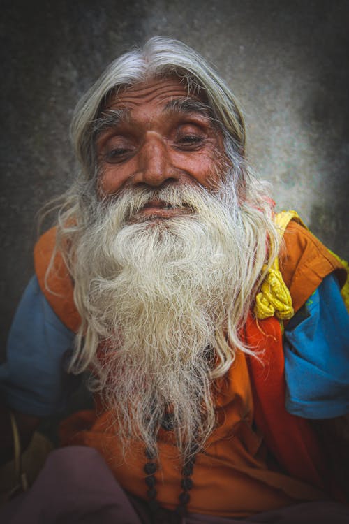 Friendly senior Indian male with wrinkled skin and gray beard looking at camera in daylight