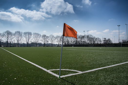Wide view of an outdoor soccer field with an orange corner flag under a clear blue sky.