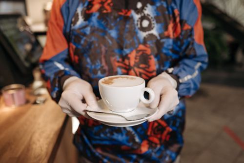 Free Cozy café setting with a barista serving a hot cappuccino on a saucer. Stock Photo