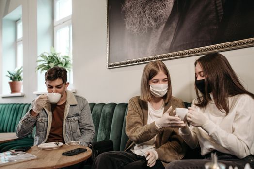 Friends wearing masks and gloves enjoying coffee together indoors, capturing a pandemic moment.