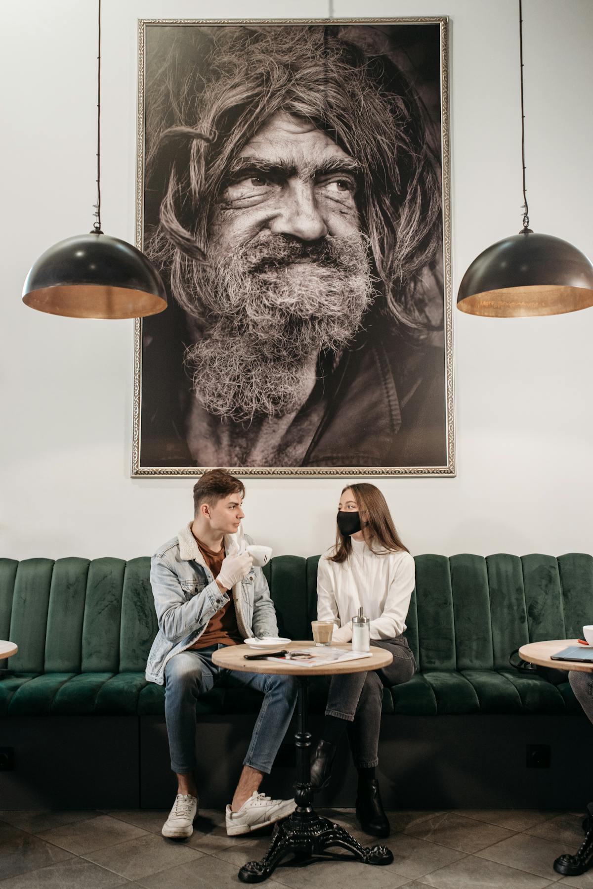 Due amici conversano in un caffè sotto un grande ritratto.