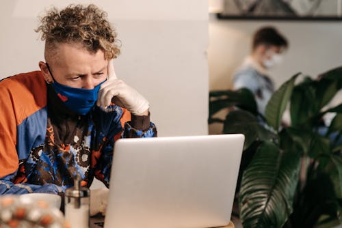 Free Man Wearing Blue Face Mask Using a Laptop Stock Photo