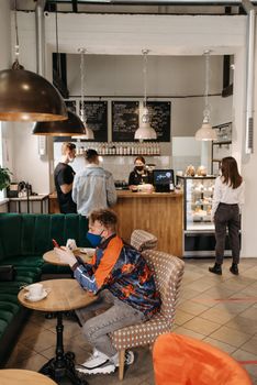 A man in a café wearing a face mask, browsing on his phone, signifying pandemic life.
