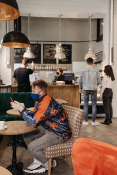 Man in a café wearing a face mask while using a smartphone, capturing modern pandemic lifestyle.