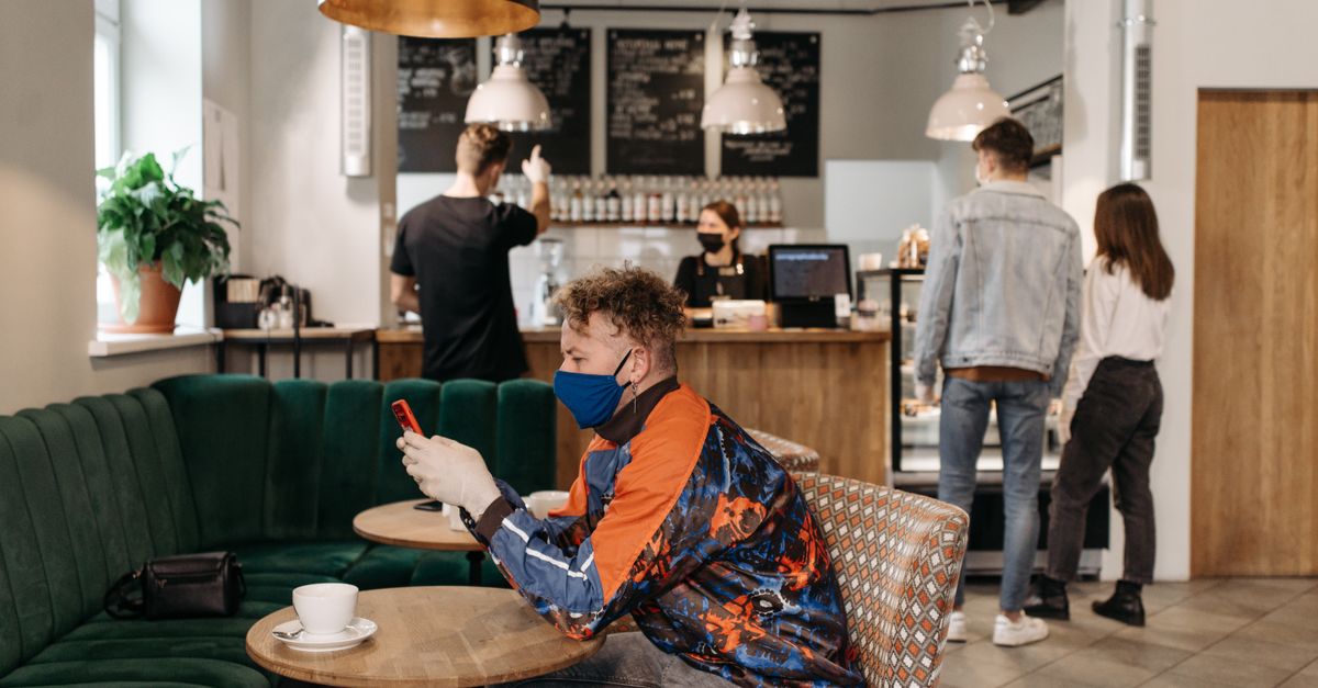 A person sitting alone in a cafe, looking at a phone with a thoughtful expression, surrounded by other people