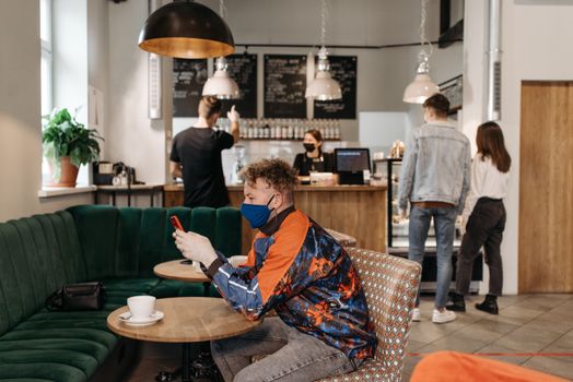 A man wearing a face mask uses his phone in a stylish café with people around.
