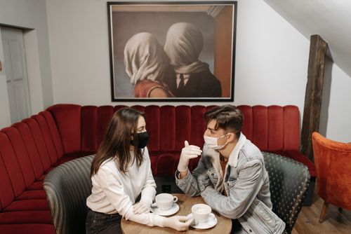 Free A couple enjoys coffee while wearing masks in a cozy café, highlighting the pandemic's impact. Stock Photo