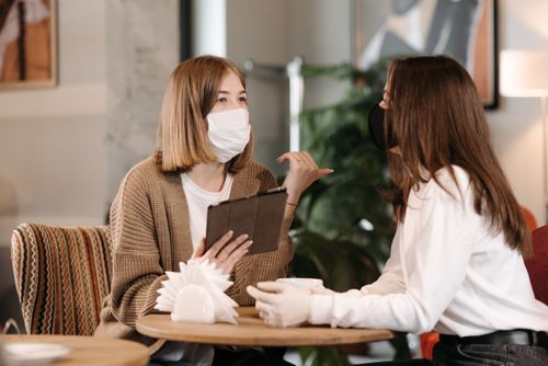 Free Two women wearing masks discussing in a café, reflecting the new normal of social interactions. Stock Photo