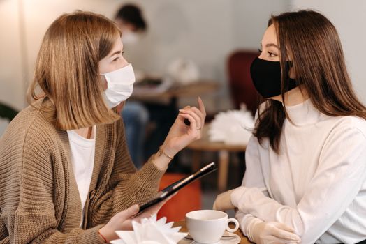 Two women wearing masks having a conversation at a café table, embracing the new normal.