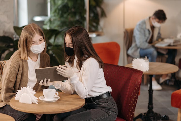 People Wearing Face Masks Looking At The Screen Of A Tablet