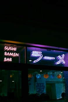 Vibrant neon lights of a sushi and ramen bar with illuminated paper lanterns, captured at night.