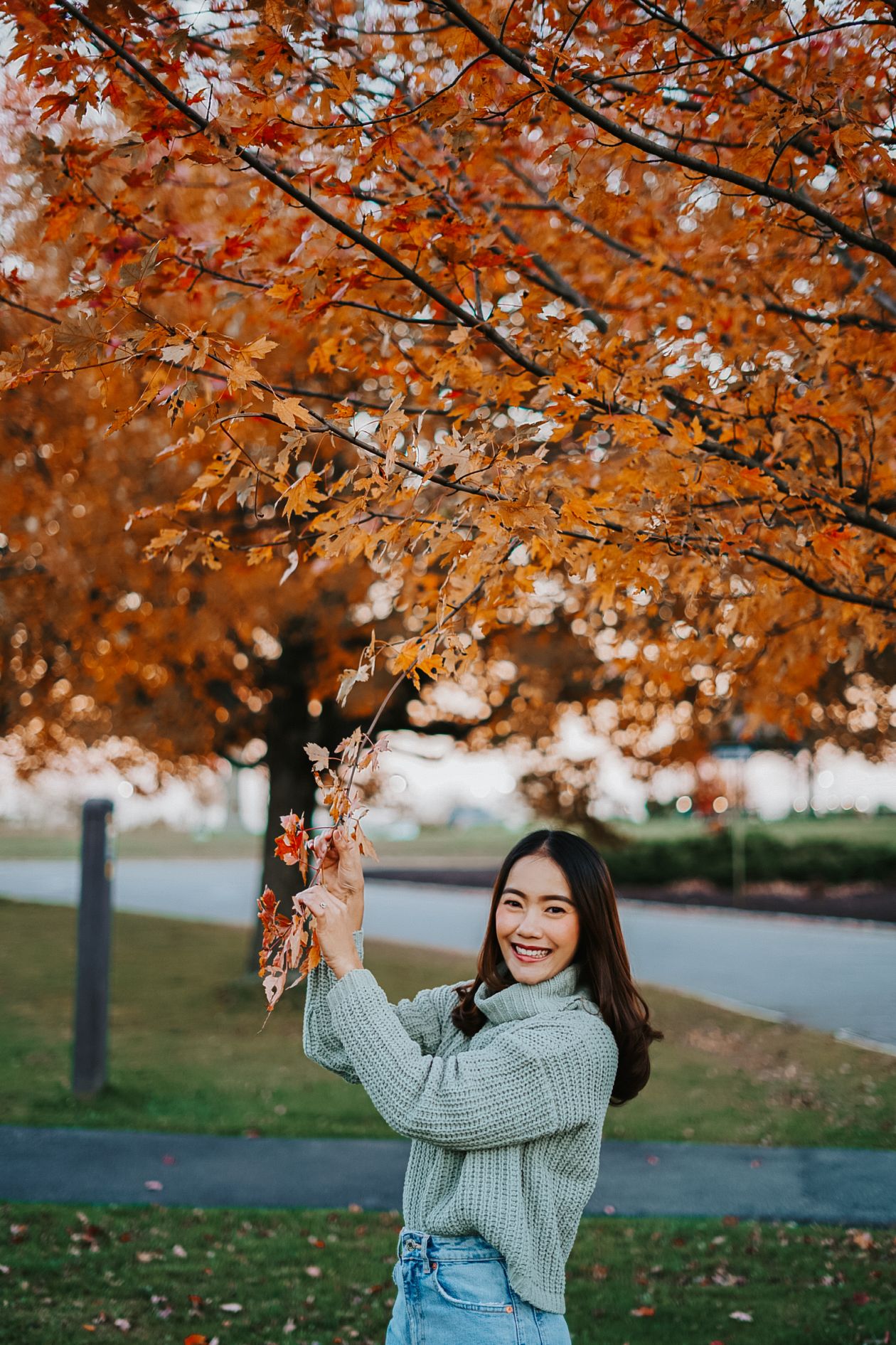 Chica asiática sonriendo rodeada de hojas de otoño