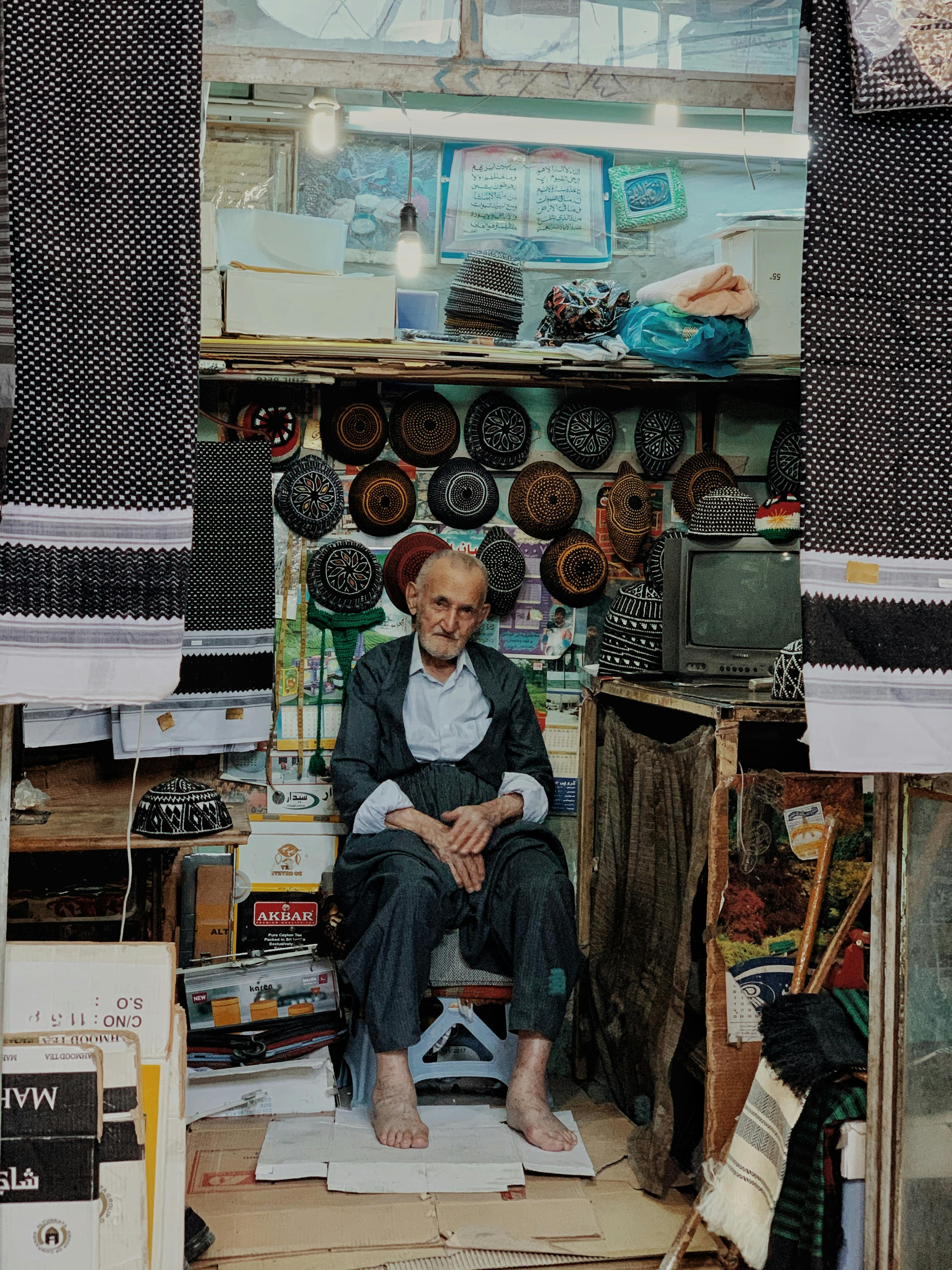senior man sitting near traditional caps on bazaar