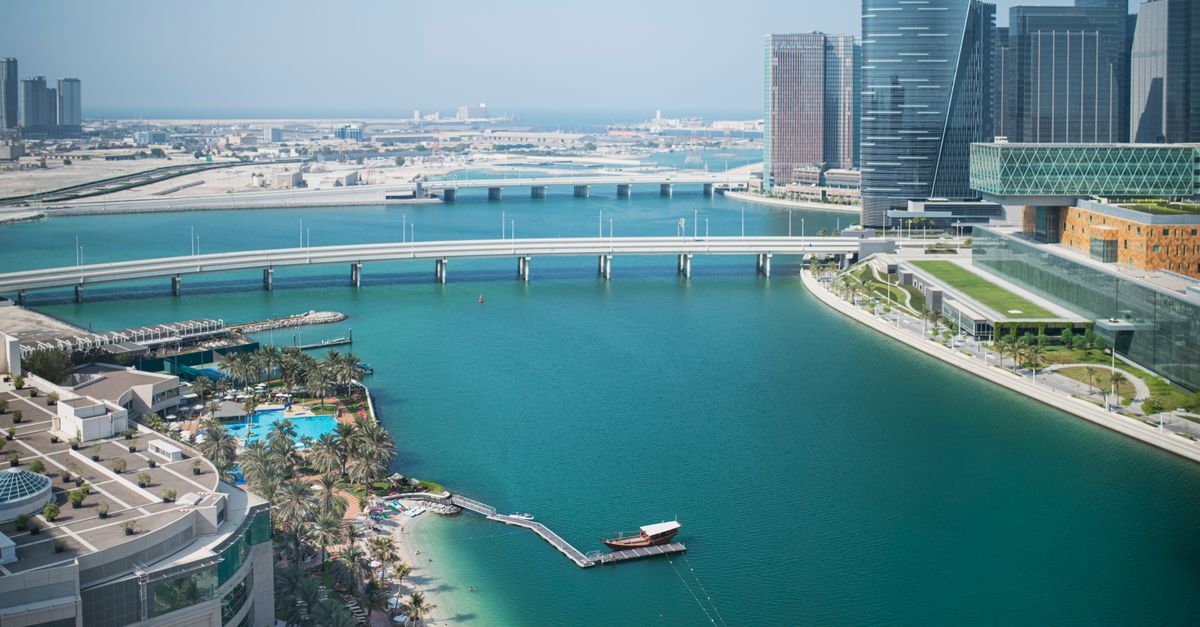 Cityscape of modern skyscrapers located near calm water in harbor on summer sunny day under blue cloudless sky