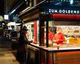 Colorful street food vendor at night in Vienna's bustling city streets, featuring neon lights and engaging interactions.