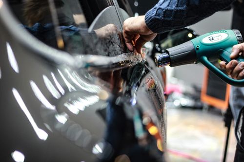 Free Close-up of a worker using a heat gun for car detailing in an indoor garage setting. Stock Photo
