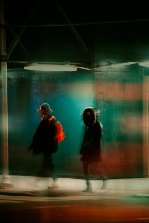 Unrecognizable people on pavement near road and building at night