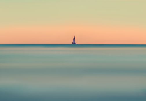 A lone sailboat on a calm ocean with a vivid, tranquil sunset backdrop.