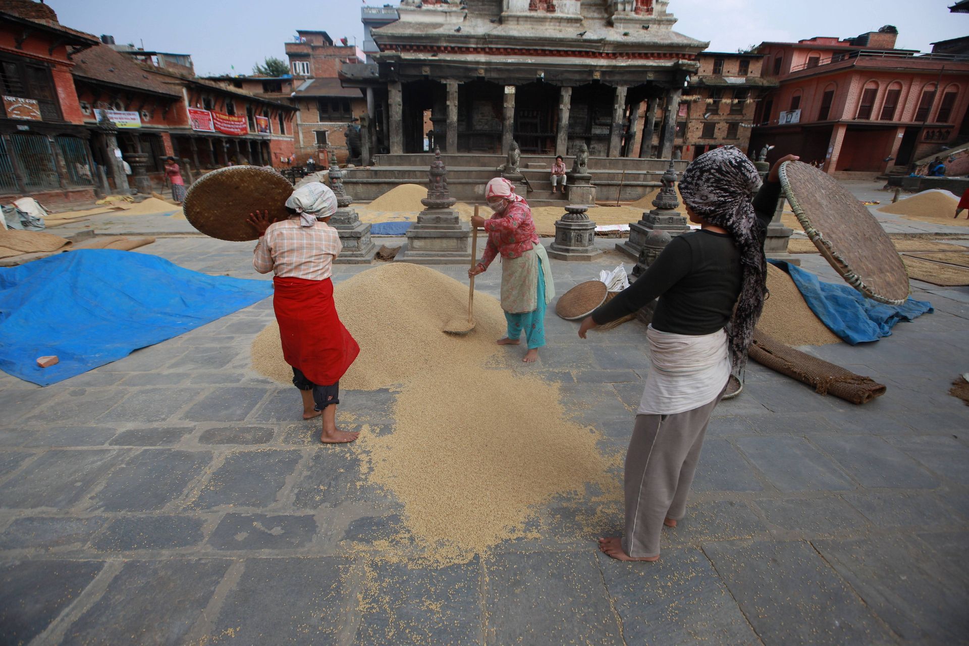 Anonymous ethnic female in traditional wear sifting rice with sieves on square against old city buildings