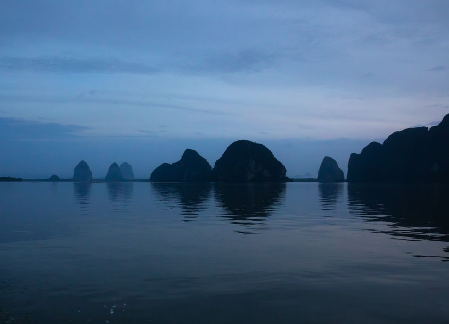 Atmospheric seascape of limestone karsts in Thailand at twilight, reflecting in calm waters.