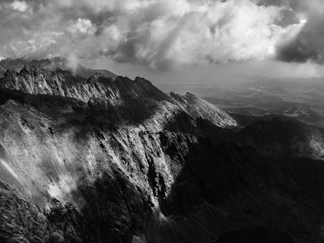 A stunning black and white photograph capturing the rugged peaks and dramatic clouds of Vysoké Tatry mountains.