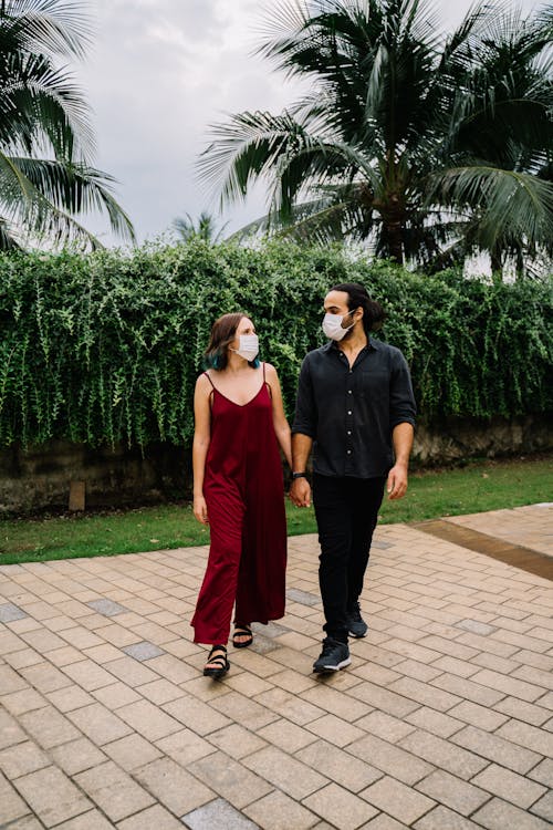 Free Couple Wearing Face Masks Holding Hands While Walking Stock Photo
