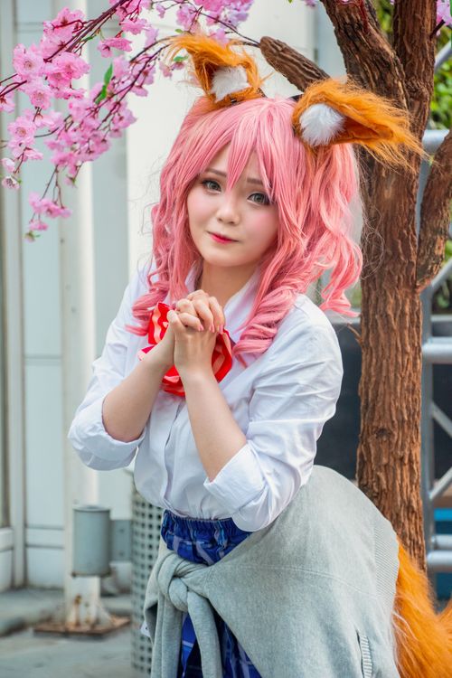 Free Charming cosplay portrait featuring a woman with pink hair and fox ears, standing by cherry blossoms. Stock Photo