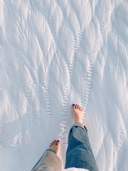 Adult woman walking barefoot in soft, snowy terrain, capturing serene winter atmosphere.